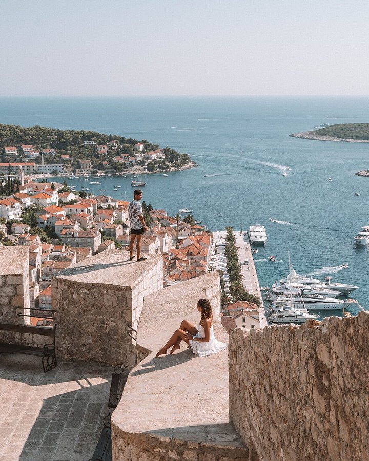 2 people standing on a ledge looking at the croatian sea and boats
